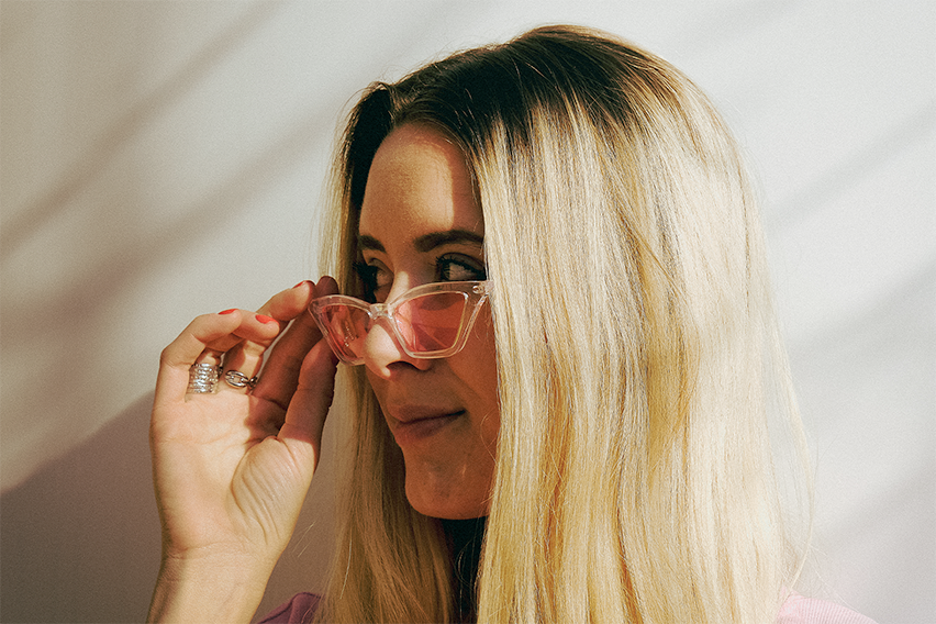 White girl with blond hair and pink glasses looking side way