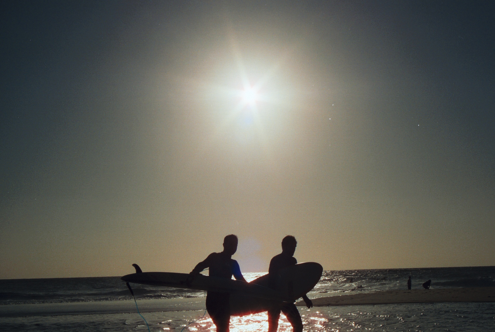 2 surfers, backlit in front of the ocean during a sunset.